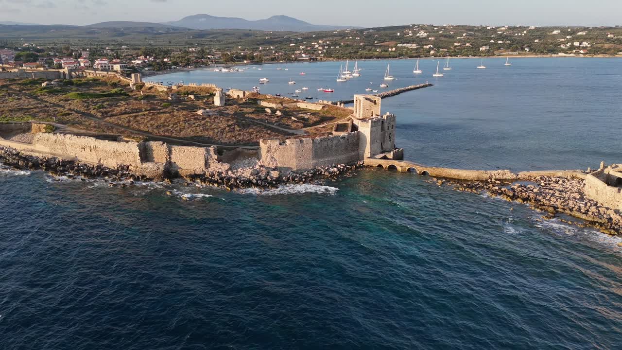 Methoni,Messenia,Peloponnese,Aerial view forward from Bourtzi Tower towards Methoni Castle surrounded by the sea during golden hour. Background are hills and beautiful landscape.Waves crush over rocks