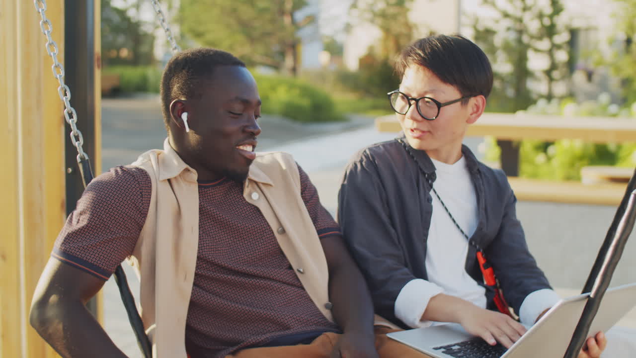 흑인 남성과 아시아 여성이 노트북과 함께 스에 앉아 이야기하고 있습니다.