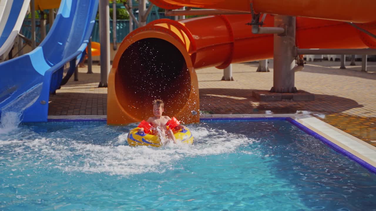 Sliding down on waterslide. Boy playing at waterpark pool going down on waterslide