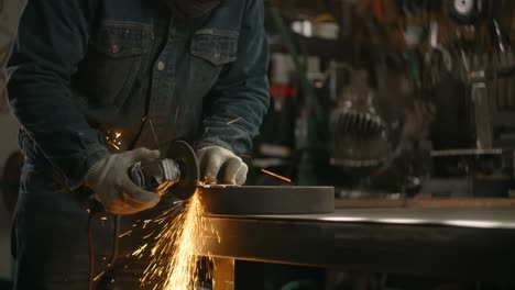 locksmith in safety face mask sands the edges of a metal detail by electric grinder with a lot of sparks in slow motion, metalwork at workshop, 4k 60p prores hq