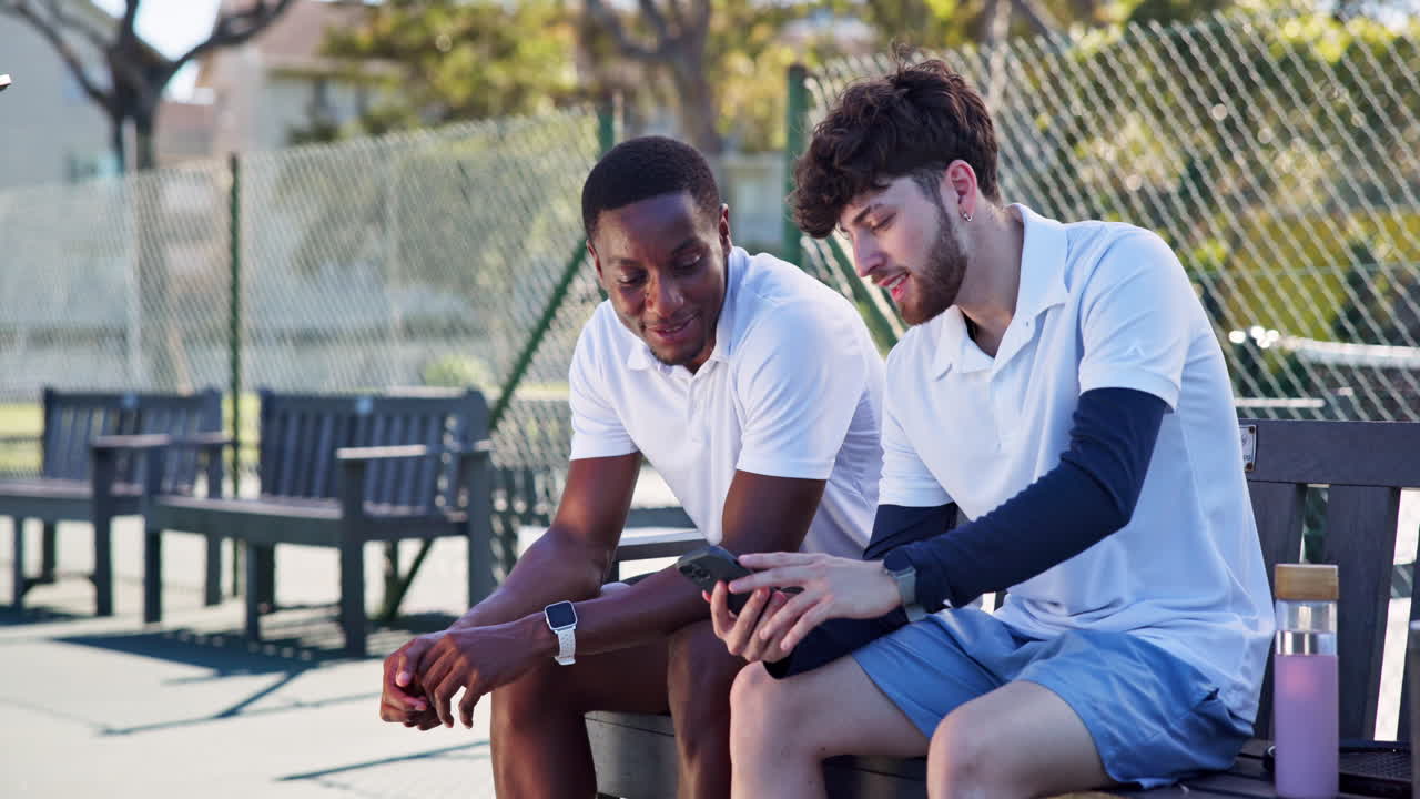 Two Young Tennis Players Relaxing on Bench and Using Smartphone