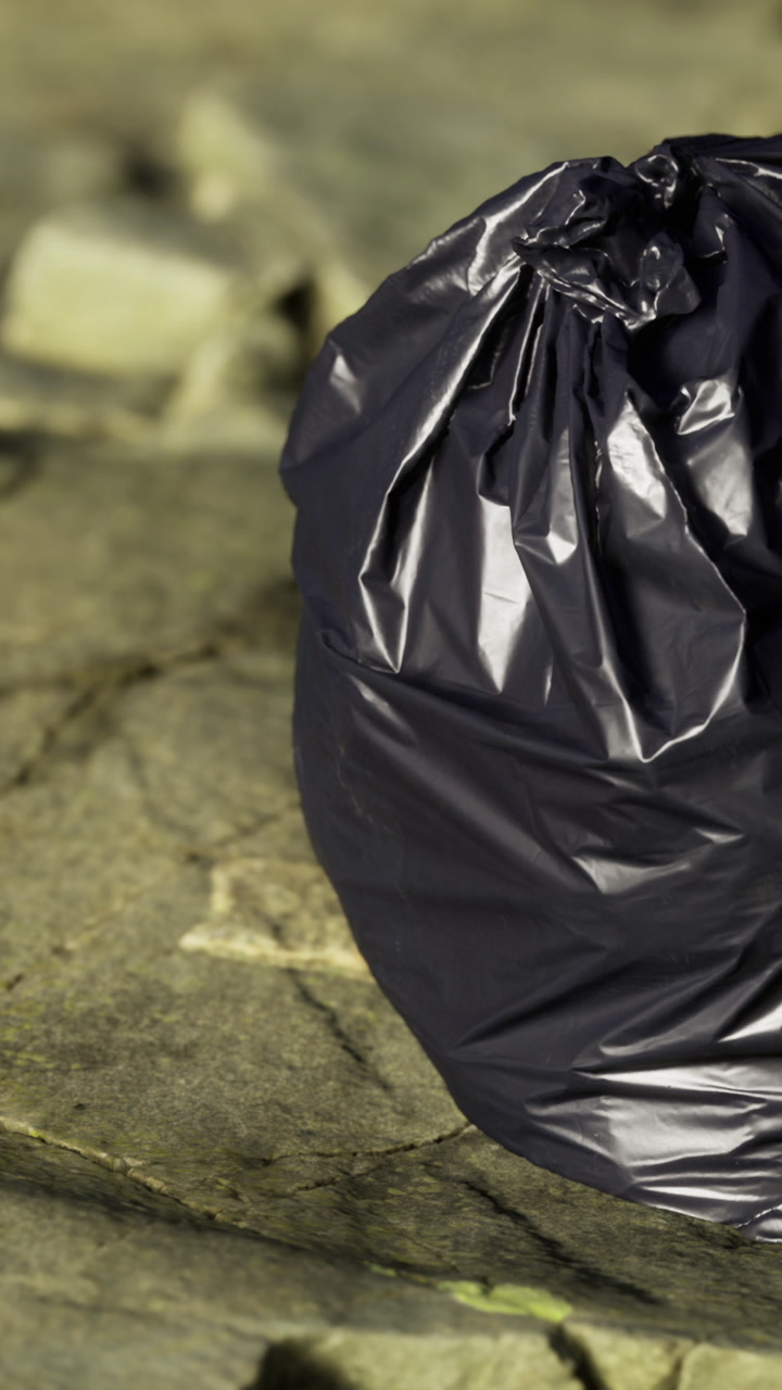 Black garbage bag placed on cracked pavement near urban area at dusk