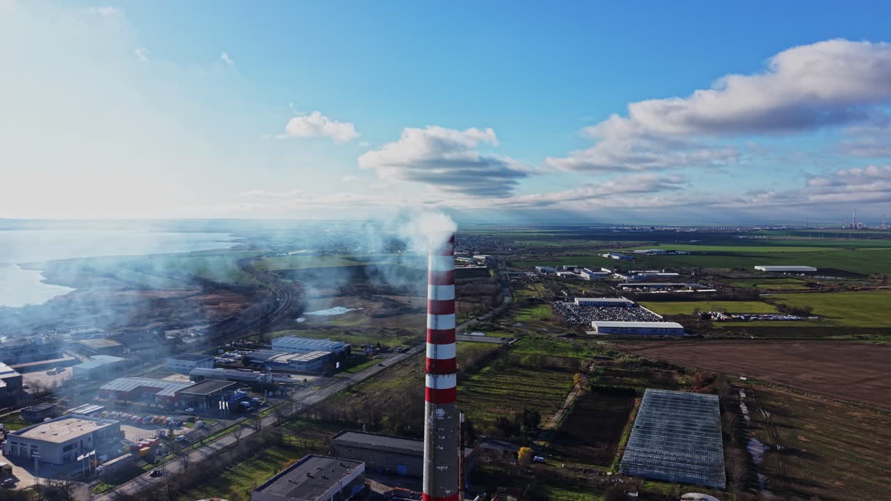 Fumo che si alza da un'alta ciminiera vicino a campi e fabbriche durante il giorno