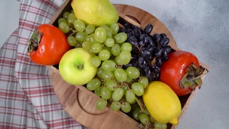 circular rotation a box with fresh fruits - grapes, lemon,apple, pear, persimmon ,top view.