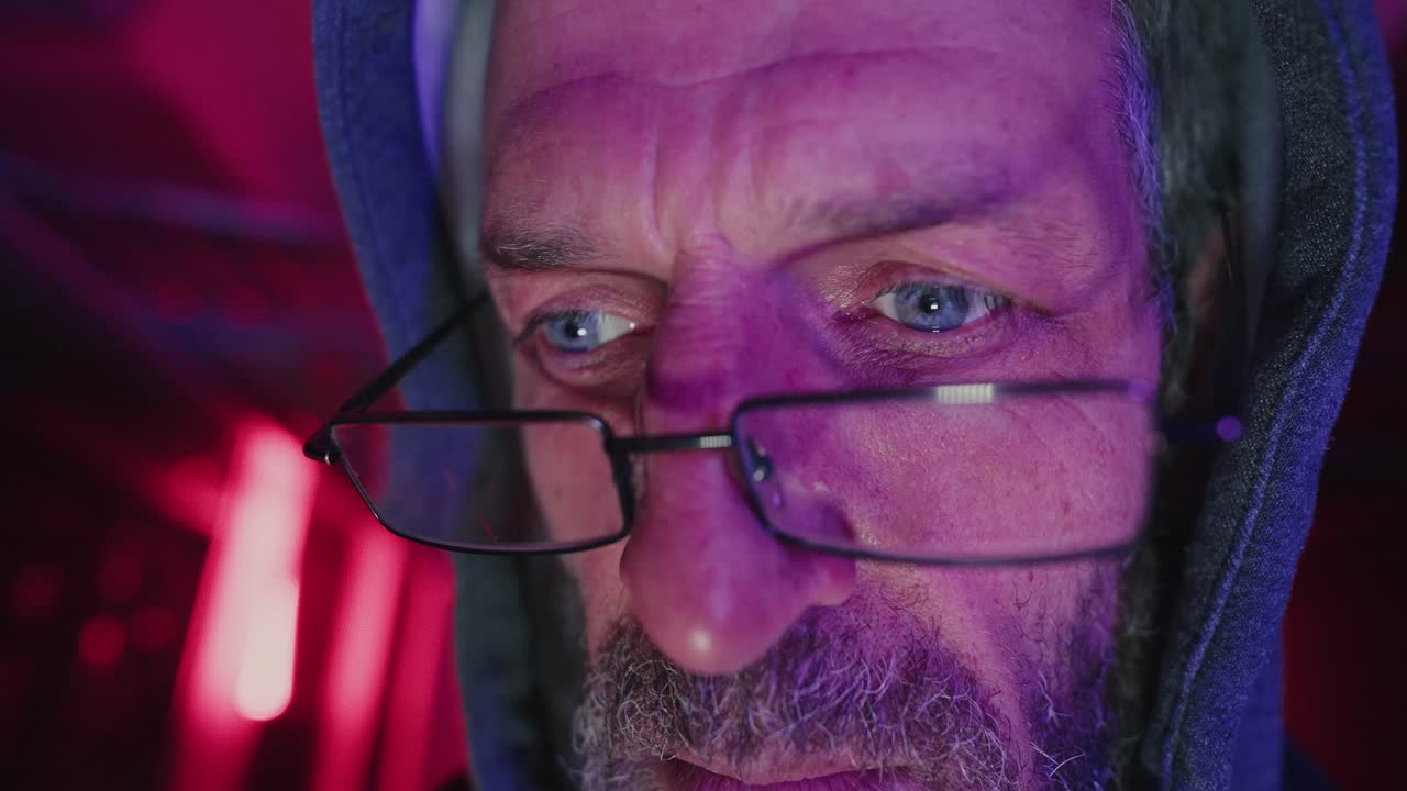 Close-up portrait of a man wearing a hoodie and glasses in a dimly lit room