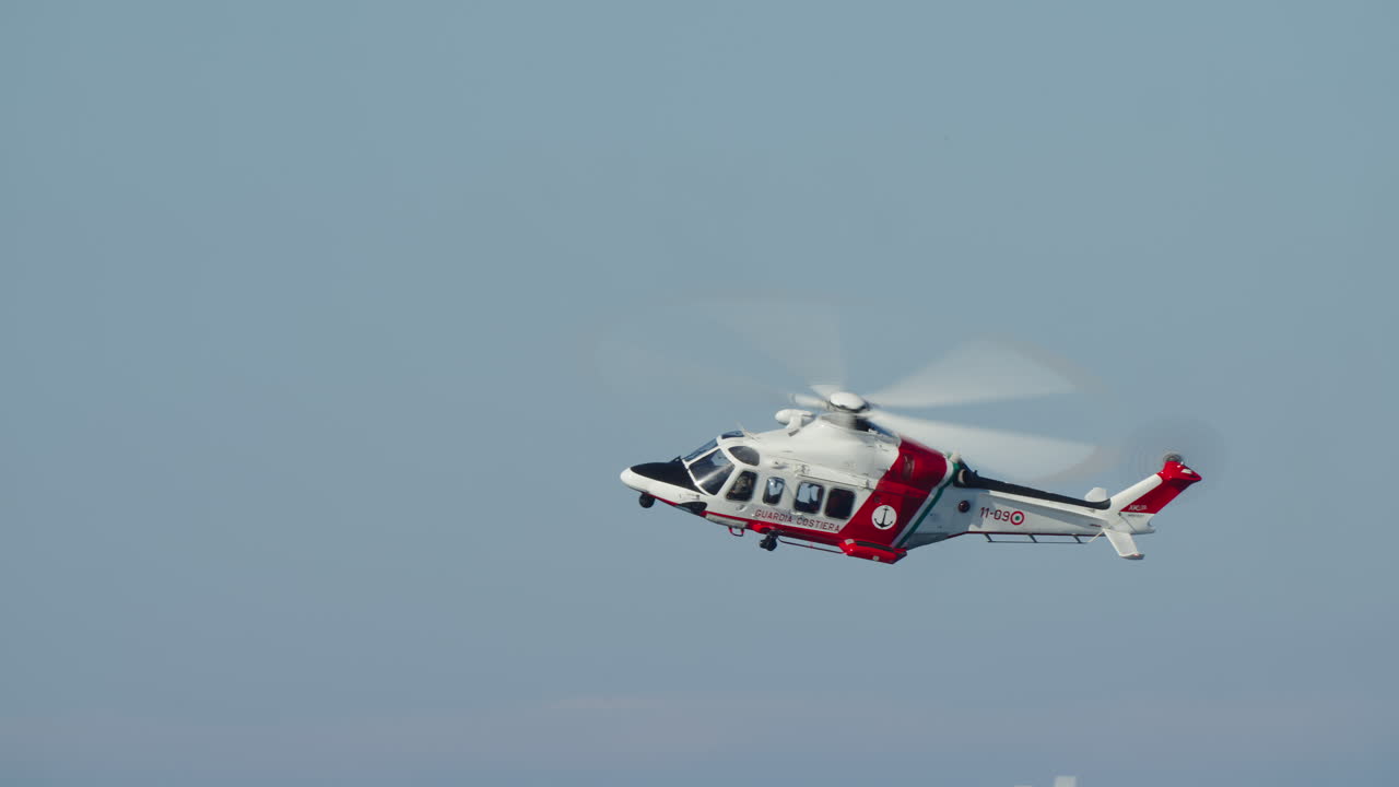 Hvid og rød kystvagthelikopter flyver på en klar blå himmel