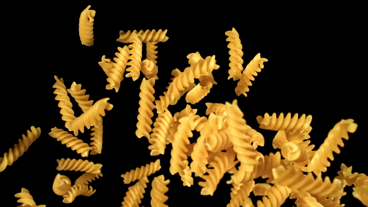 Massa fusilli seca caindo e subindo em câmera lenta em fundo preto.