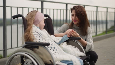 madre feliz sostiene la mano de la hija pequeña en silla de ruedas