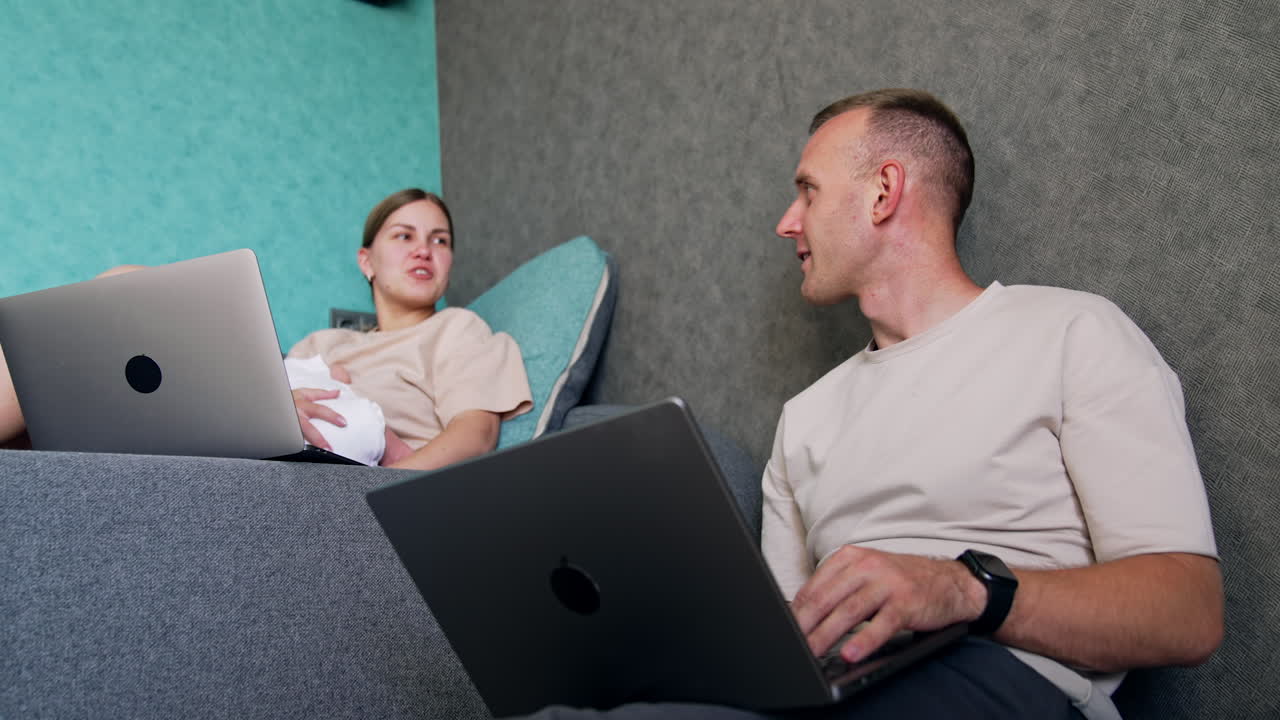 Caucasian parents work on laptops sitting at home. Couple with newborn child using laptops. Low angle view.