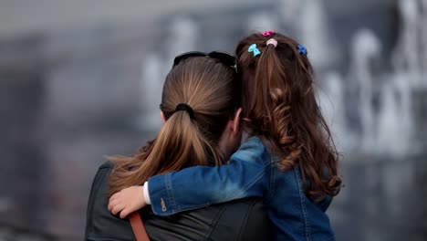 niña sosteniendo a su madre mientras mira y toma una foto de la fuente de agua