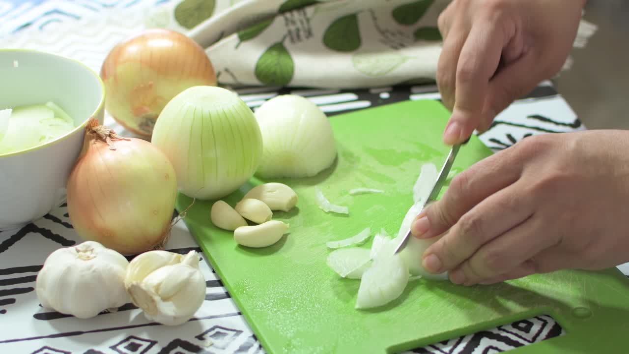 Brunette woman's hands cutting onion slices, on a green cutting board, on a kitchen table. Preparing a salad.