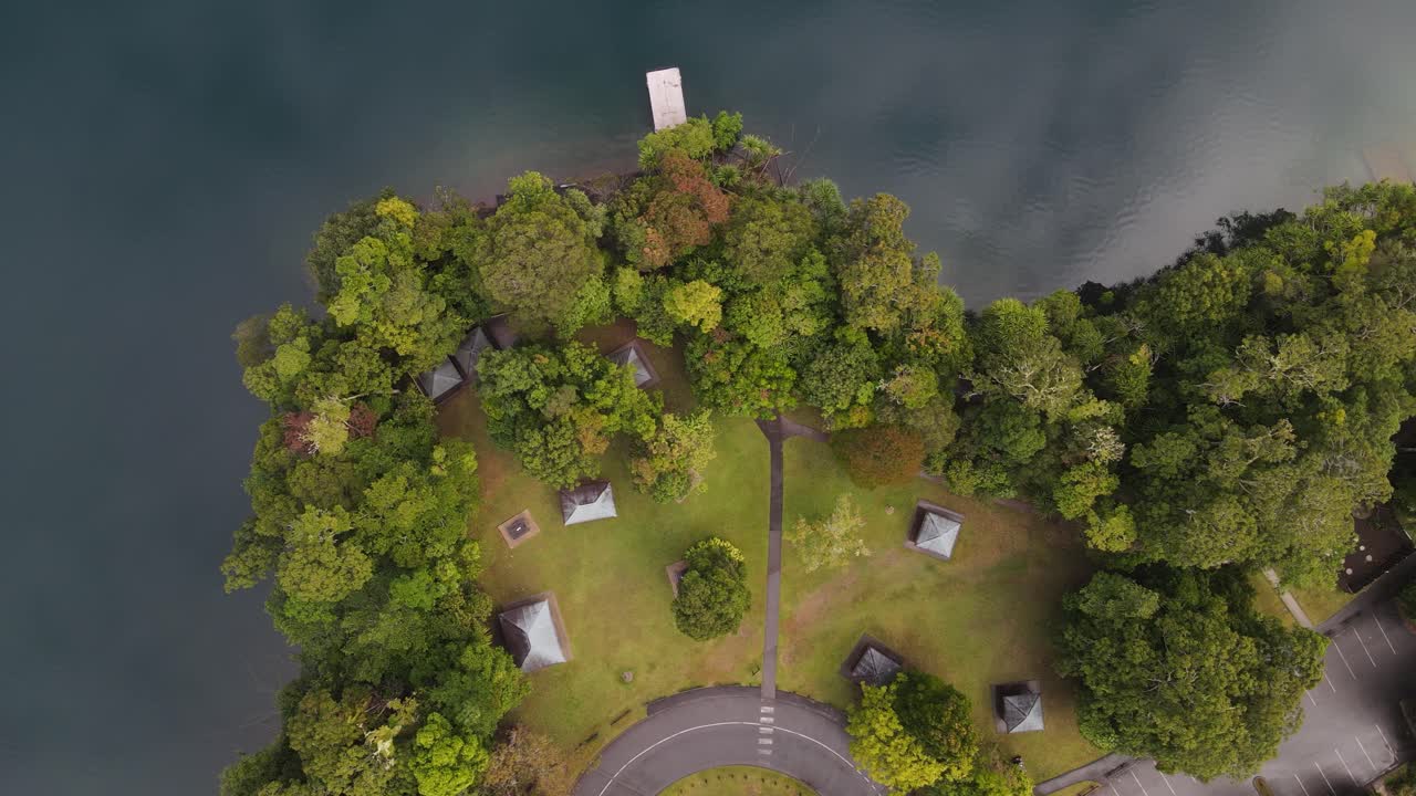 Pohyblivé video z dronu shora na svěží parkovou oblast vedle jezera v sopečném kráteru s mraky odrážejícími se na klidné vodě