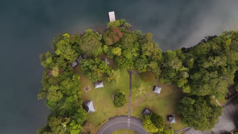 Video-De-Drones-En-Movimiento-Mirando-Hacia-Abajo-En-Un-Exuberante-Parque-Junto-A-Un-Lago-De-Cráter-Volcánico-Con-Nubes-Reflejadas-En-Las-Aguas-Tranquilas