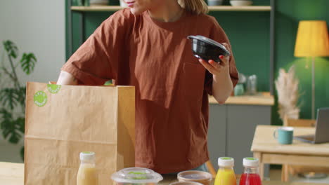 mujer joven descargando comidas y bebidas de una bolsa de papel