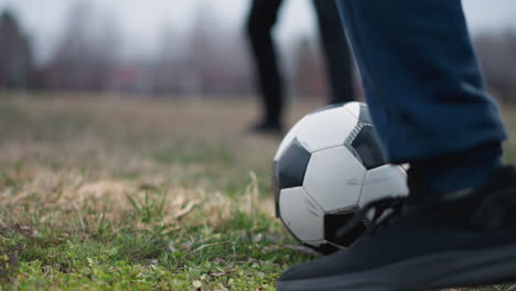 close-up of someone playing football, with another person standing close by and a blurred background featuring people passing by