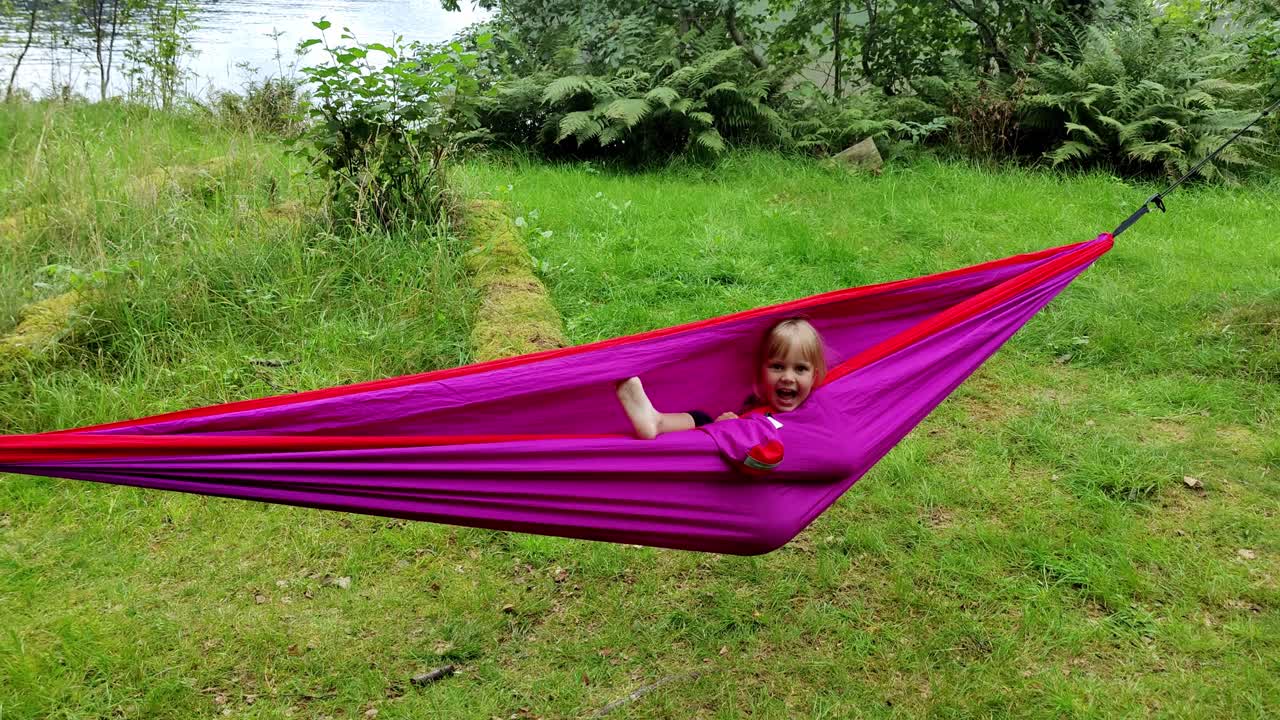 Playful young girl laughing and having fun inside purple hammock - Handheld clip of girl enjoying nature hiking trip - Norway
