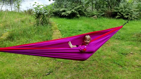playful young girl laughing and having fun inside purple hammock - handheld clip of girl enjoying nature hiking trip - norway