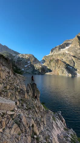 4k, figura vertical de una mujer de pie en una roca por encima de un hermoso lago glacial en un soleado día de verano, panorama