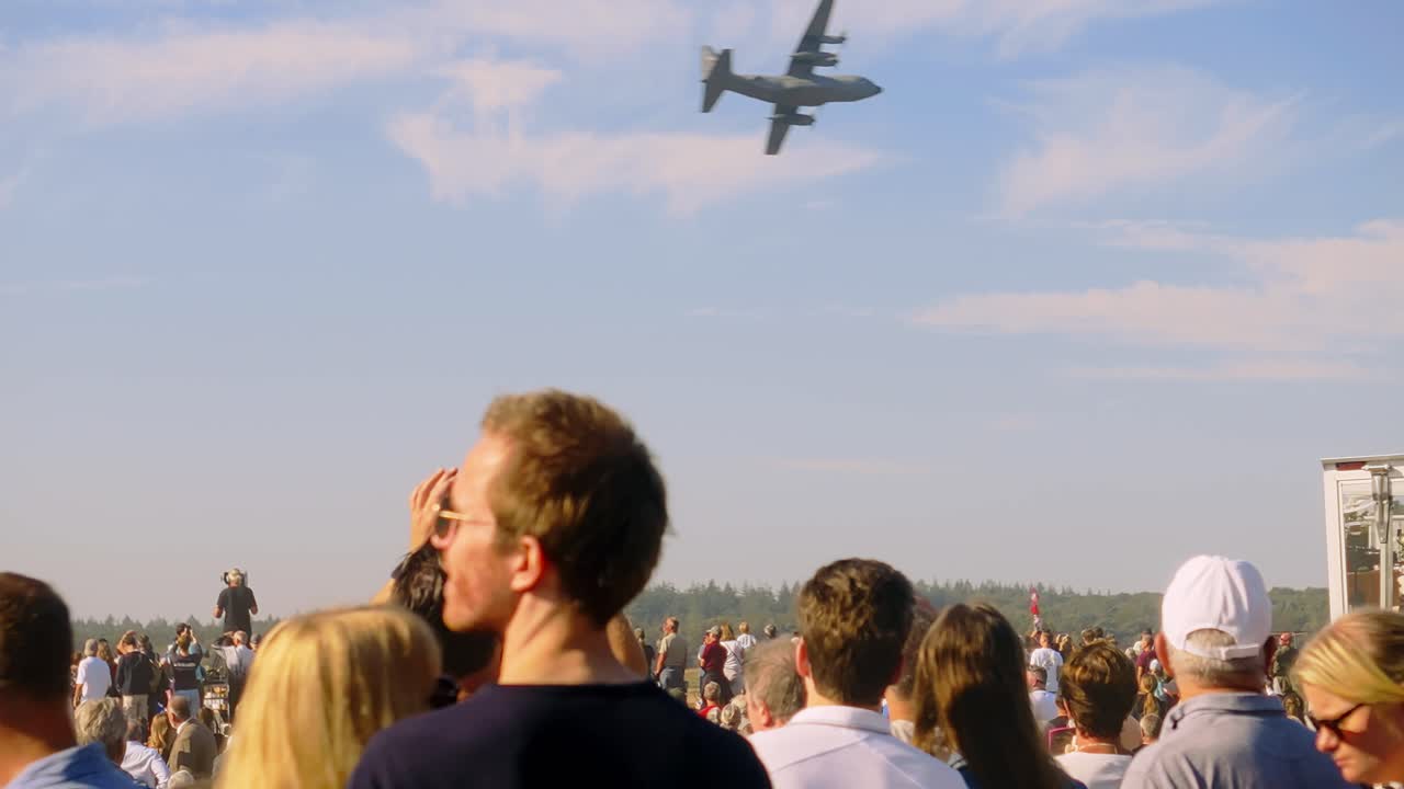 Military aircraft flying low over a large audience attending the Airborne event at Ginkelse Heide, Netherlands. Intense atmosphere and awe-inspiring aerial display as crowd watches the plane pass by.