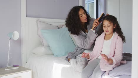 Happy-mixed-race-mother-and-daughter-brushing-hair-in-bedroom