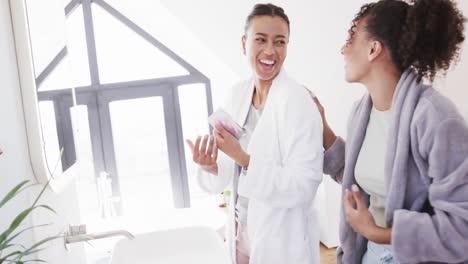 Happy-biracial-lesbian-couple-in-bathrobes-embracing-in-sunny-bathroom-in-the-morning,-slow-motion