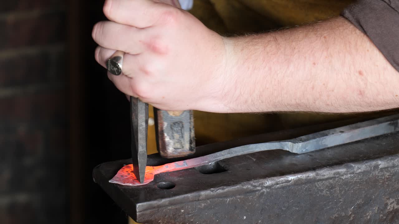 Blacksmith stokes a coal fire and pounds a red hot peice of metal with a hammer