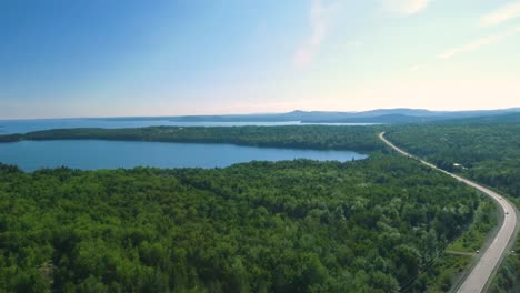 Disparo-De-Un-Dron-Que-Se-Eleva-Y-Revela-Un-Enorme-Lago-Junto-A-Una-Carretera-Boscosa