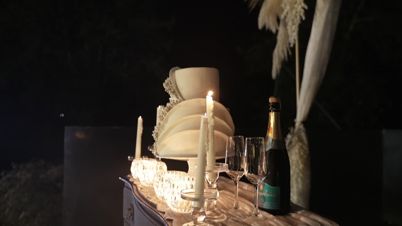 Table with elegant decor including lit candles, champagne bottle, and a multi-tiered cake