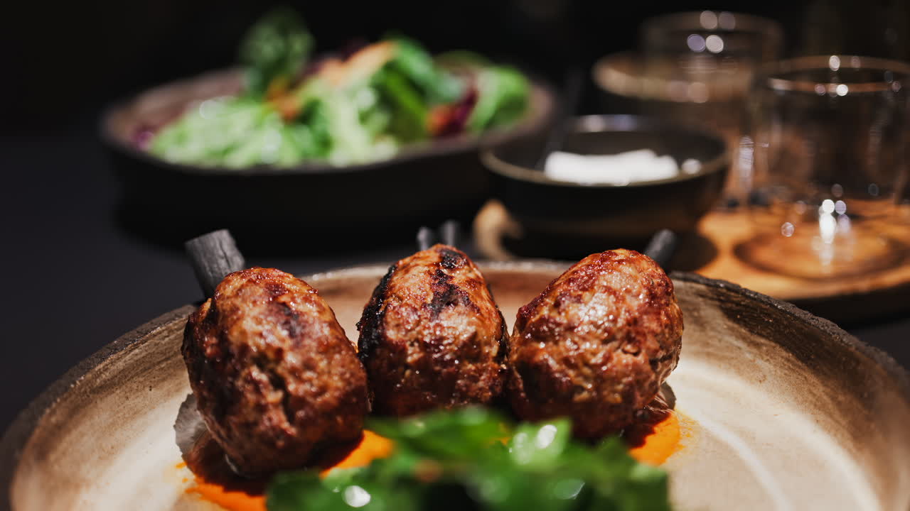 Three grilled meat skewers on charcoal sticks served on a plate with an orange sauce