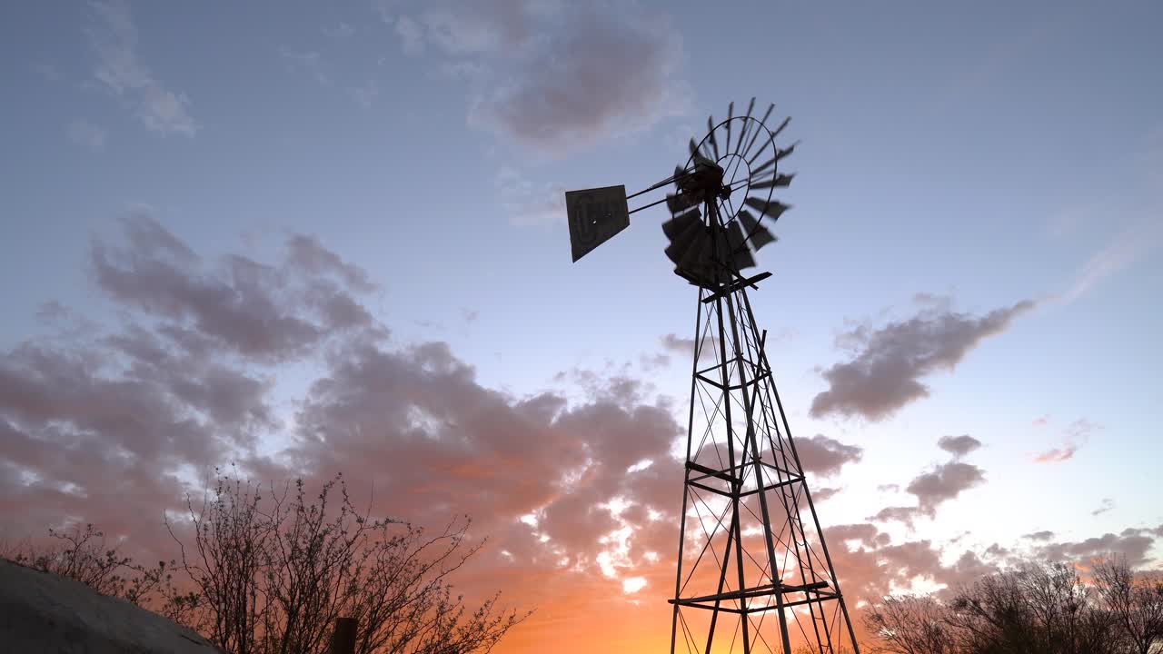 Windpump against a dramatic sunset with orange clouds on a sheep farm near Keetmanshoop, Namibia. Stable wide shot.