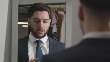joven con traje en casa practicando la técnica de la entrevista de trabajo reflejada en el espejo usando el teléfono móvil 1