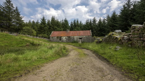 time lapse of field road leading to abandoned farmhouse surrounded by forest on a cloudy summer day in ireland