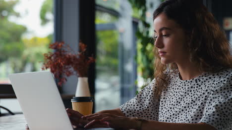 Joven-Empresaria-Con-Café-Para-Llevar-Trabajando-Sentada-En-Una-Computadora-Portátil-En-Una-Cafetería