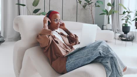 una joven afroamericana independiente se sienta en una silla con una computadora portátil en el regazo