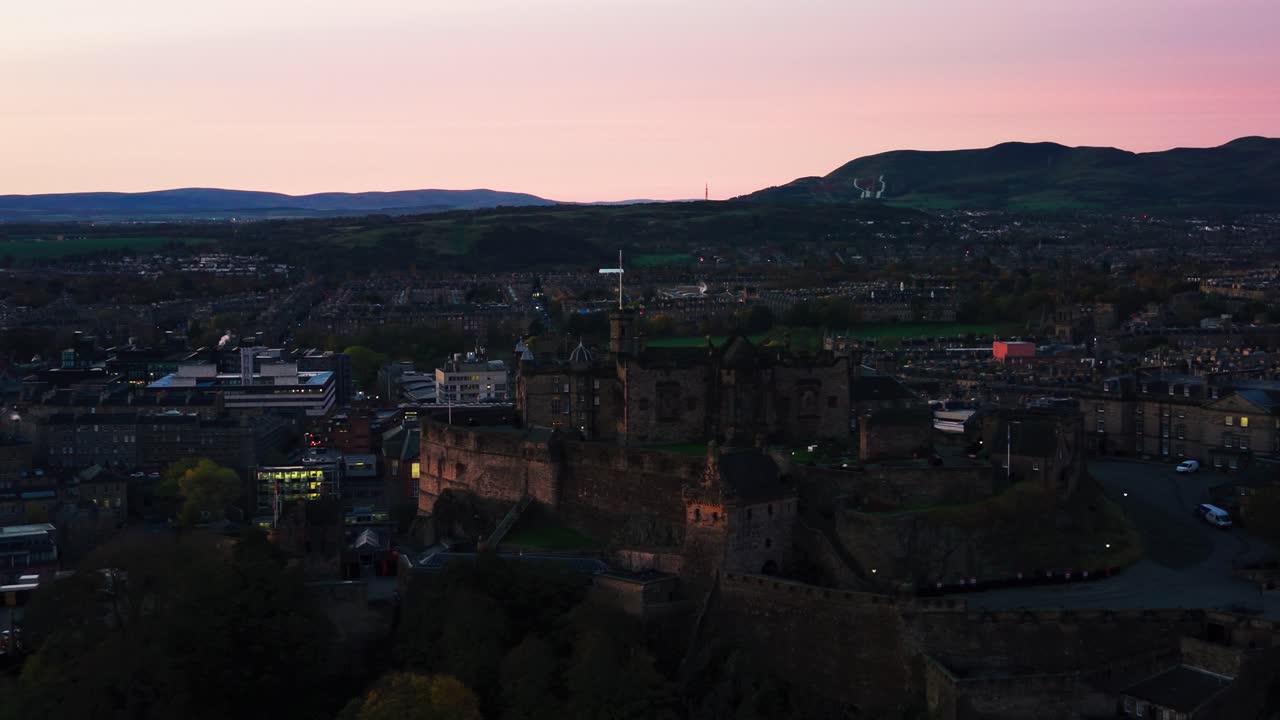 Vista drone del Castello di Edimburgo all'alba con un cielo rosa tenue sopra la città e le colline circostanti alla luce del primo mattino