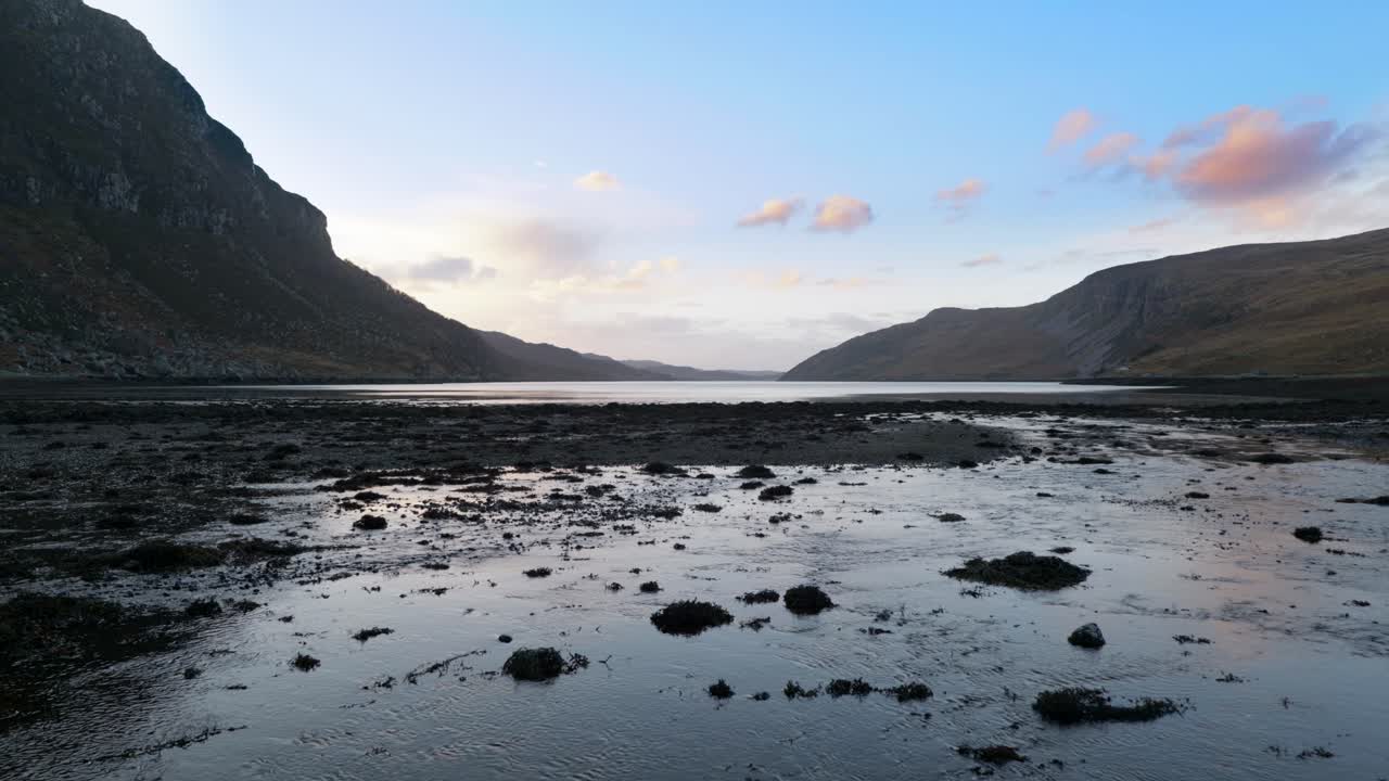 Water slowly flows into a sea loch at low tide in the highlands of Scotland at sunset, surrounded by mountains