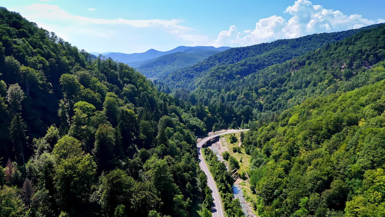 Beautiful mountain valley landscape with winding road. Lush green trees surround a winding road through a mountainous valley under a bright blue sky