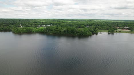 Vista-Aérea-En-Cámara-Lenta-Del-Lago-Cubierto-De-Bosque-En-Un-Lado,-Con-Un-Reflejo-Del-Cielo