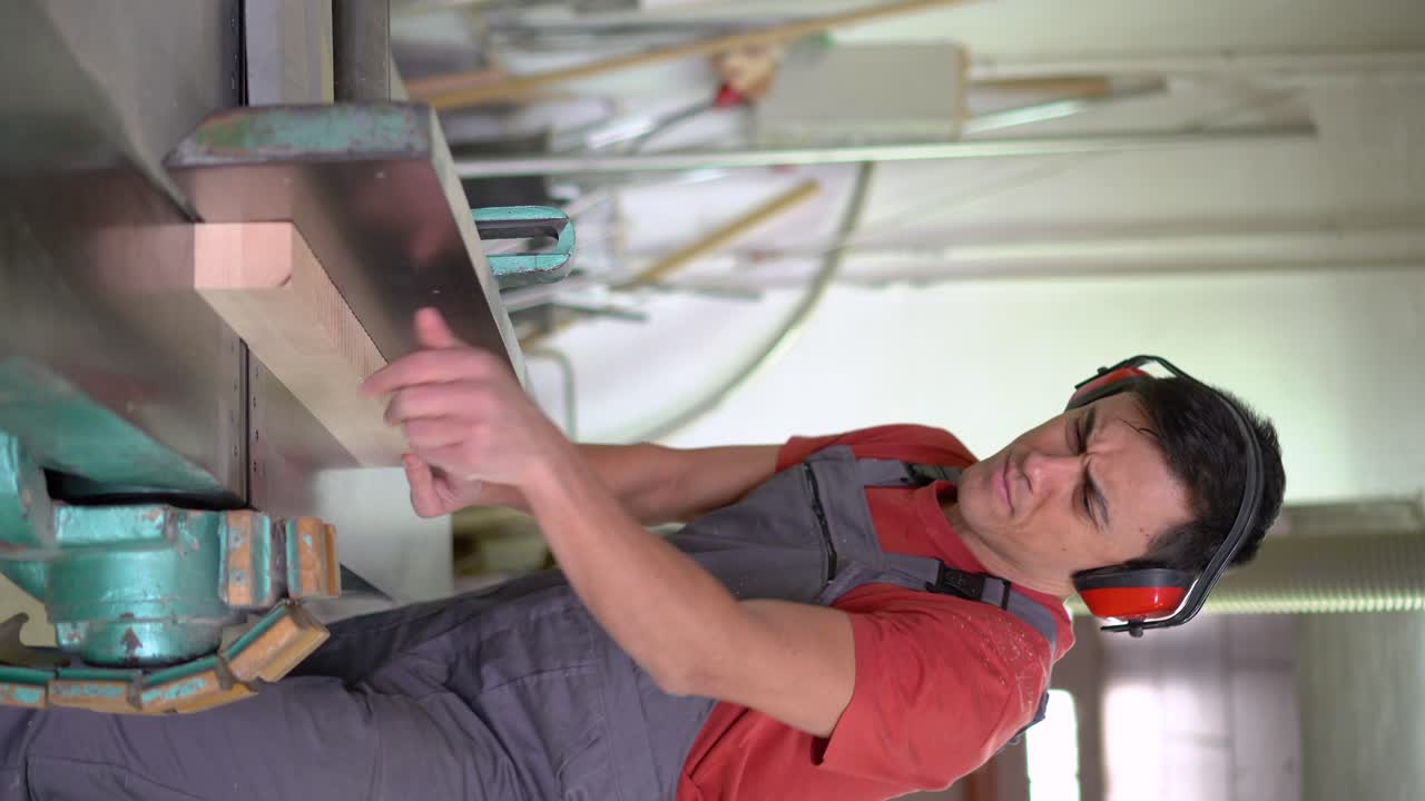 Man operating a woodworking machine with ear protection in a workshop