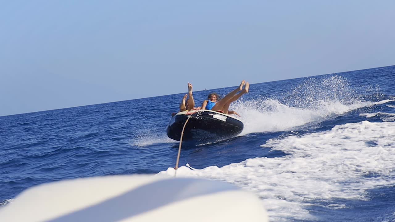two people falling off a water sports doughnut being pulled by a boat on a sunny day in the middle of the ocean