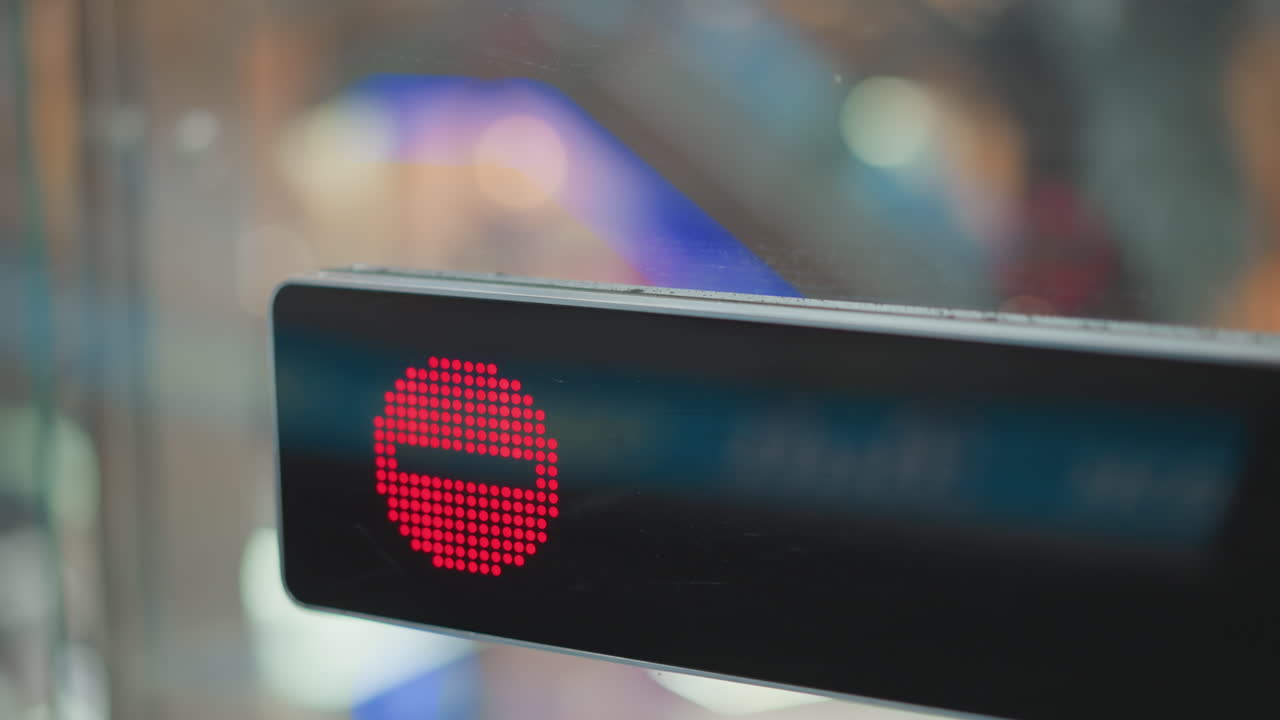 close up red stop indicator on glass panel at moving walkway entrance with blurred mall interior and reflective surfaces signaling pedestrians to halt movement on transit walkway path