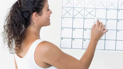 mujer caucásica sonriente marcando cruces en días de enero en el calendario mensual