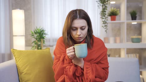 Mujer-Joven-Enferma-Envuelta-En-Pique-Tomando-Café-En-El-Sofá,-Temblando-De-Frío.