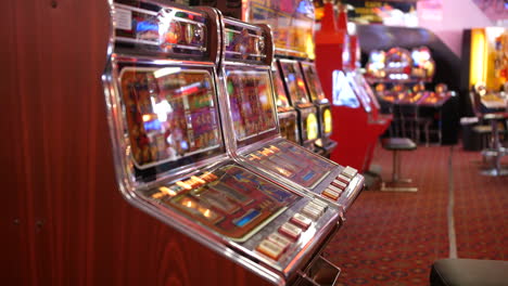 a row of colorful slot machines is lined up in a dimly lit casino arcade, reflecting bright lights and vibrant graphics on their gambling screens