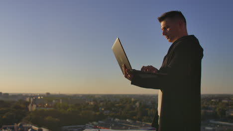 programmer a hacker is on the roof with a laptop at sunset says error code on the keyboard and looking at the city view.