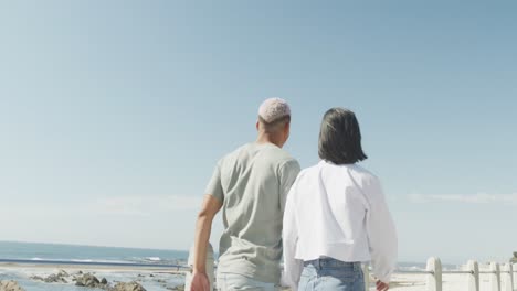 happy biracial couple walking together and holding hands on promenade, in slow motion