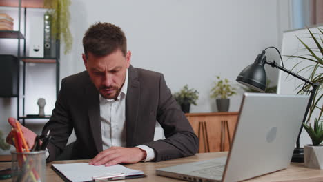 irritated angry businessman working on laptop analyzing financial graph decrease, breaking pencil