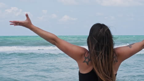 woman raising arms in front of the ocean at sunset - slow motion