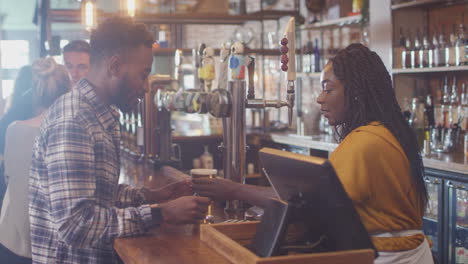 male customer in bar makes socially distanced contactless payment for drinks in health pandemic