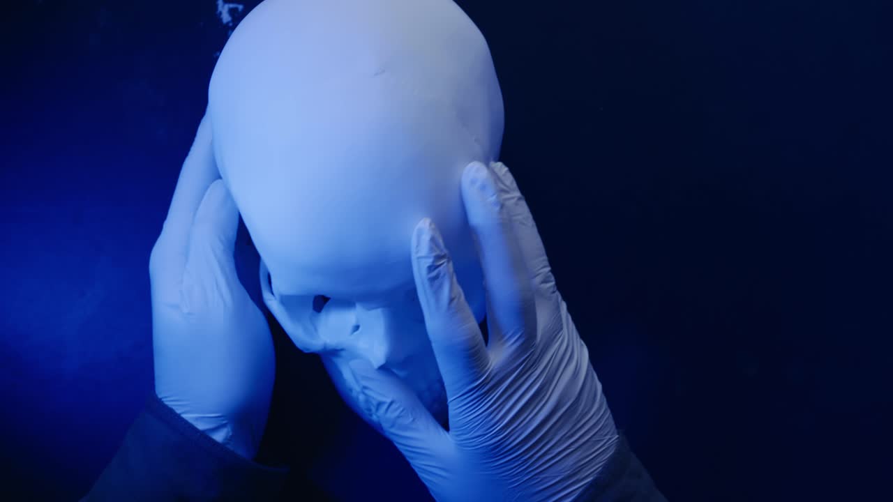 Forensic anthropologist examines human skull under blue light POV